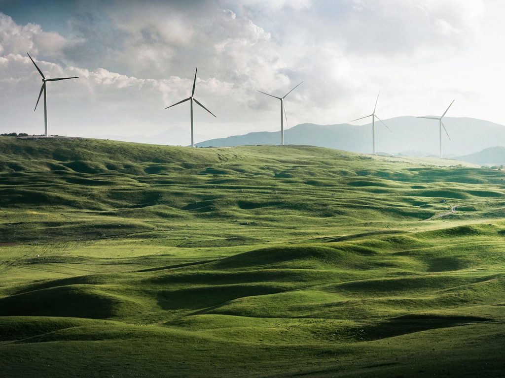 Windmills in a rolling green field overlooked by a mountain